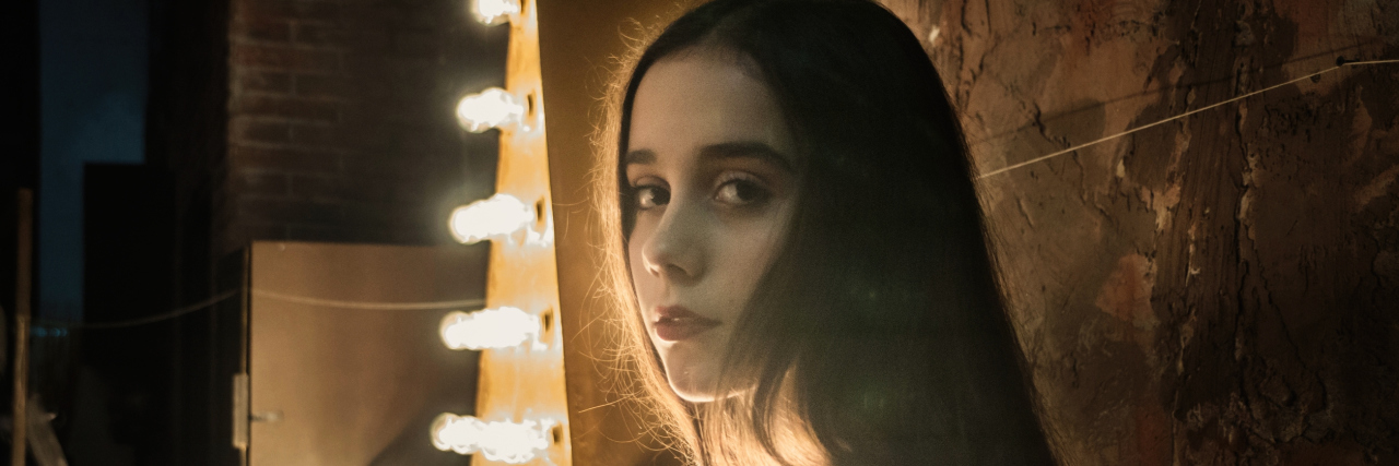 What It's Like Being a Sick Teenager in High School A young woman standing in front of a lit up sign.