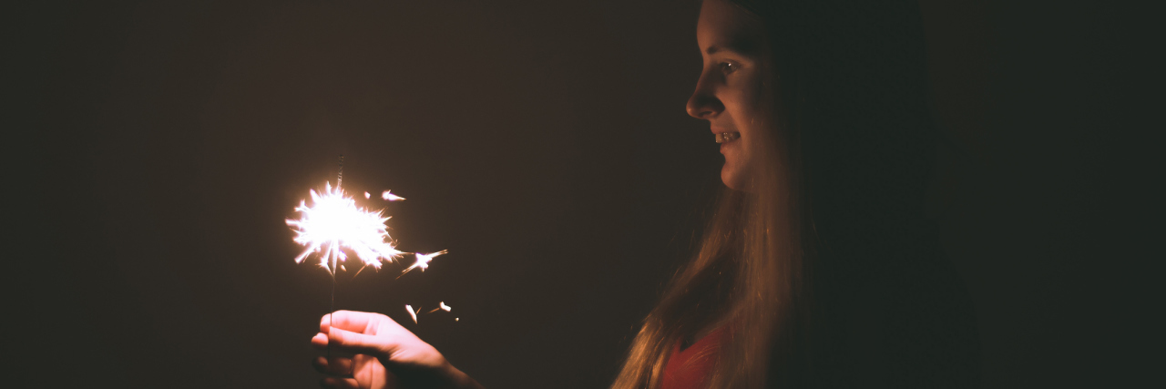 Why I Don't Make Resolutions as Someone With Chronic Illness woman holding sparkler