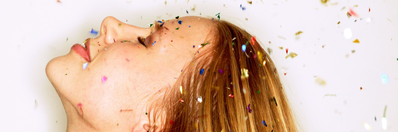 A photo of a woman looking up towards falling confetti.