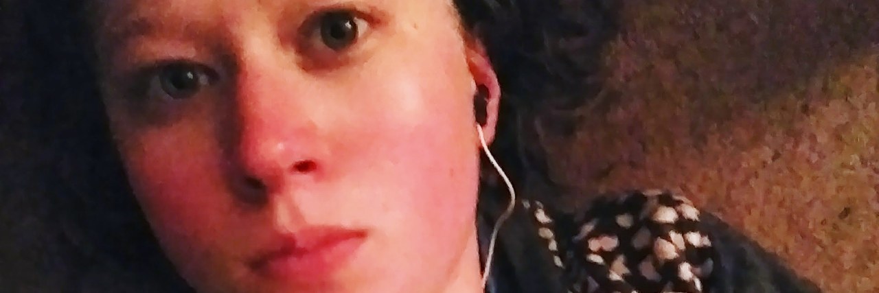 What This Photo Says About My POTS Journey A photo of the writer listening to music, laying down, with a serious facial expression.