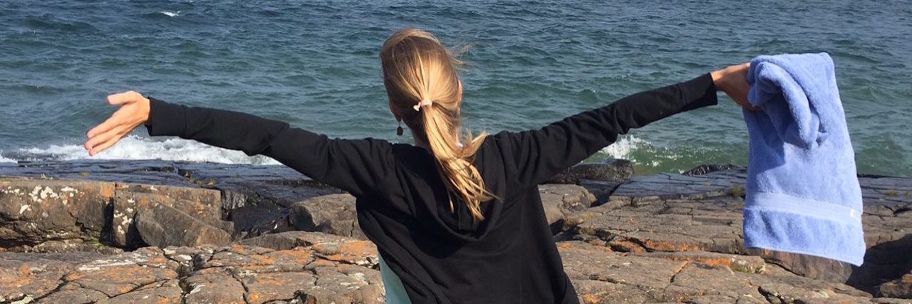 Lessons I Learned During My Year With Chronic Illness The writer by a body of water with her arms stretched out.