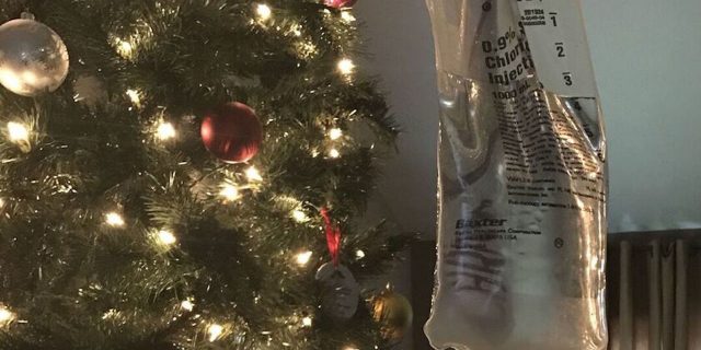 An IV pole and bag in front of a Christmas tree.