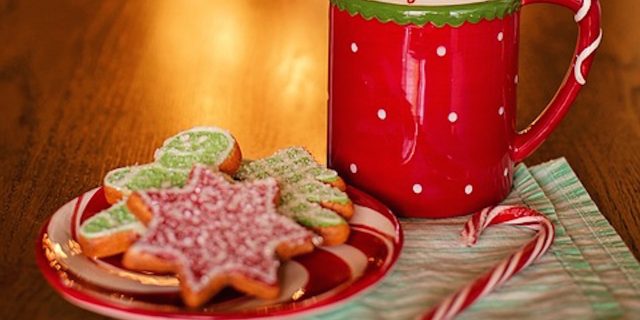 Christmas cookies and a coffee mug in front of a lit-up Christmas tree.