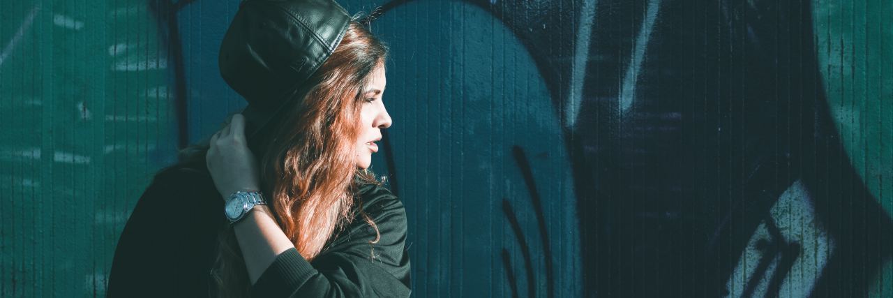 young woman in front of street art wall looking off into distance