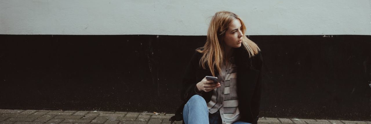 My Bad Days With 'High-Functioning' Depression a young woman sits on the streets with her phone in her hand