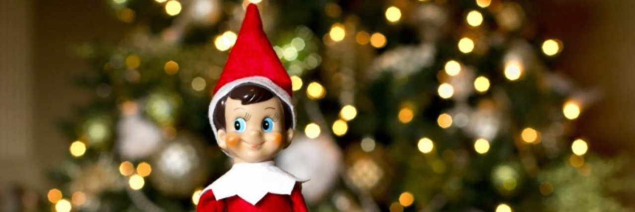 Blind Children, You May Touch Your Elf on the Shelf Elf on the shelf. Toy elf in red and white suit and Santa hat with Christmas tree in background.