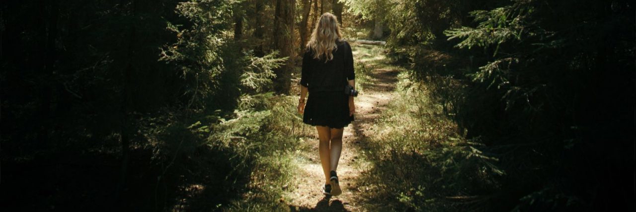 young woman walking along path through forest