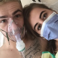A photo of the writer and her boyfriend. Her boyfriend is wearing an oxygen mask and she's wearing a medical mask.