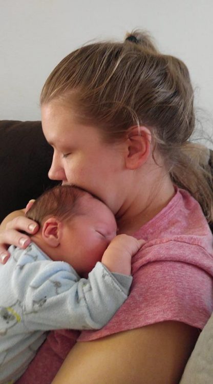 mother in a pink shirt with her hair up in a ponytail and not wearing makeup holding her newborn baby against her chest