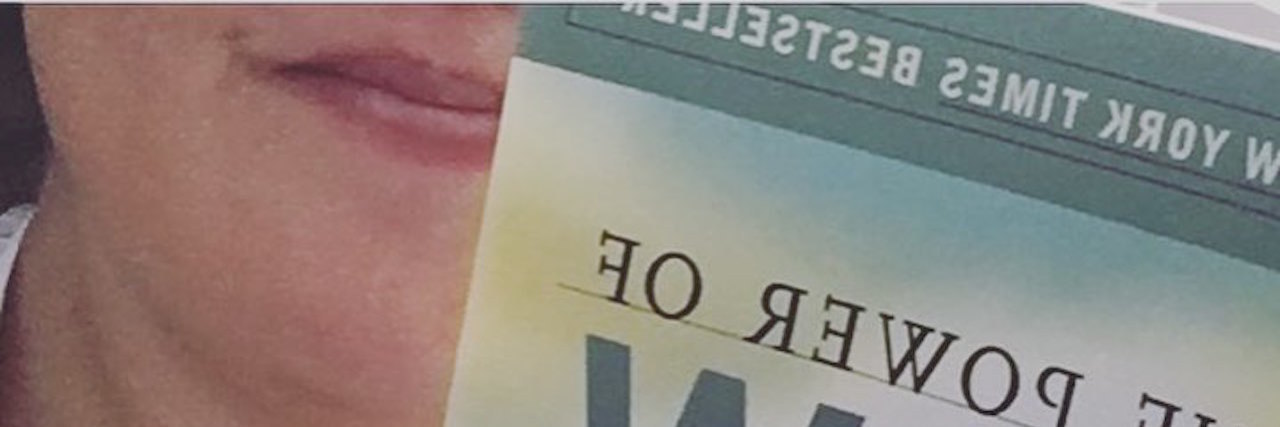 My New Year's Resolutions With Congenital Heart Disease woman wearing patterned leggings and holding a book that says "the power of now"