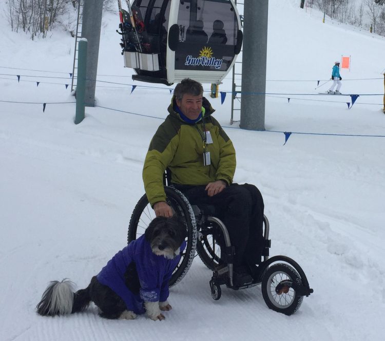 man in wheelchair in snow with freewheel wheelchair attachment on front of wheelchair