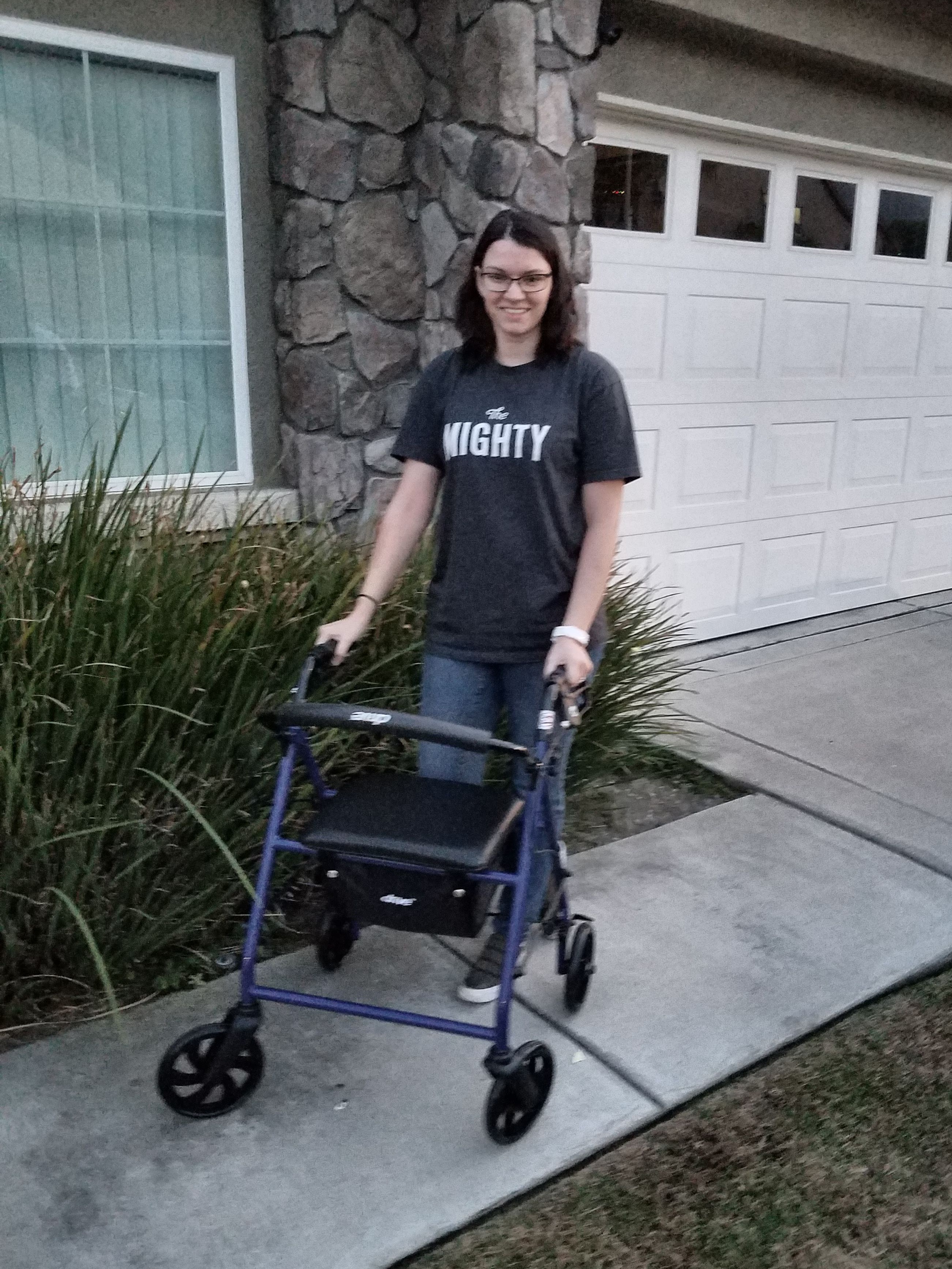 A photo of the writer standing outside with her walker, while wearing her Mighty shirt.