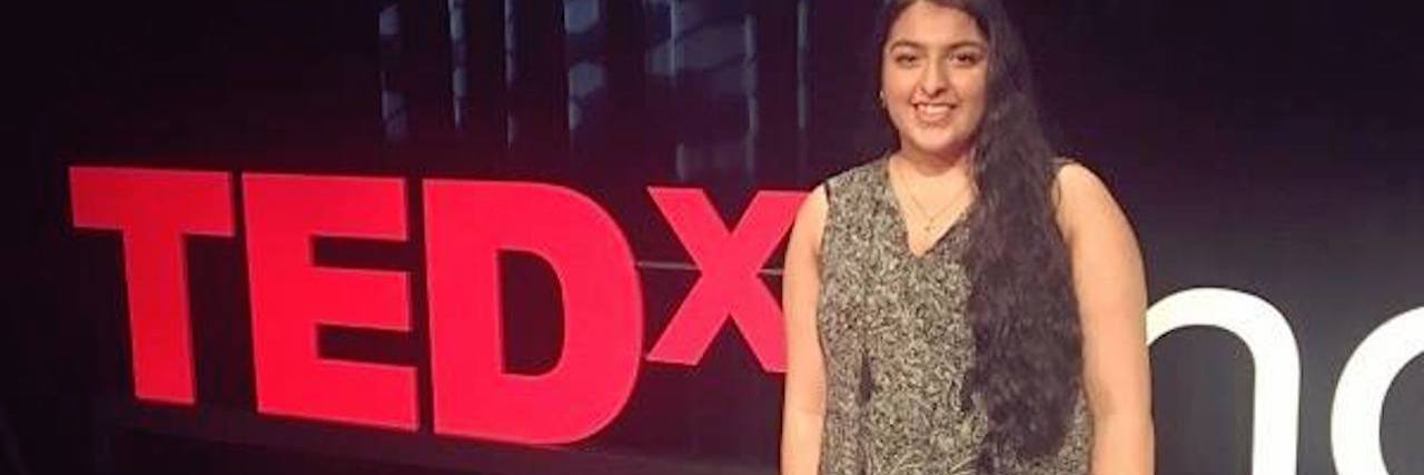 woman wearing a dress and standing in front of a TED talk sign