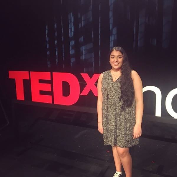 woman wearing a dress and standing in front of a TED talk sign