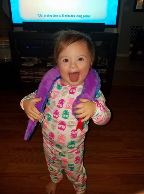 Little girl with Down syndrome wearing pajamas and a toy snake wrapped around her neck.