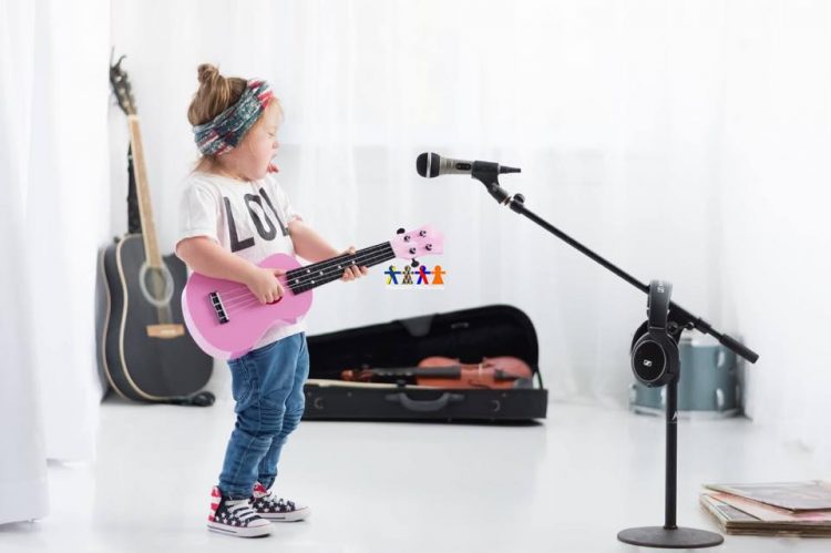 Little girl with Down syndrome in studio photo. She is holding a pink guitar, a microphone in front of her. Violin case in the background with violin inside and a guitar sitting in the corner.