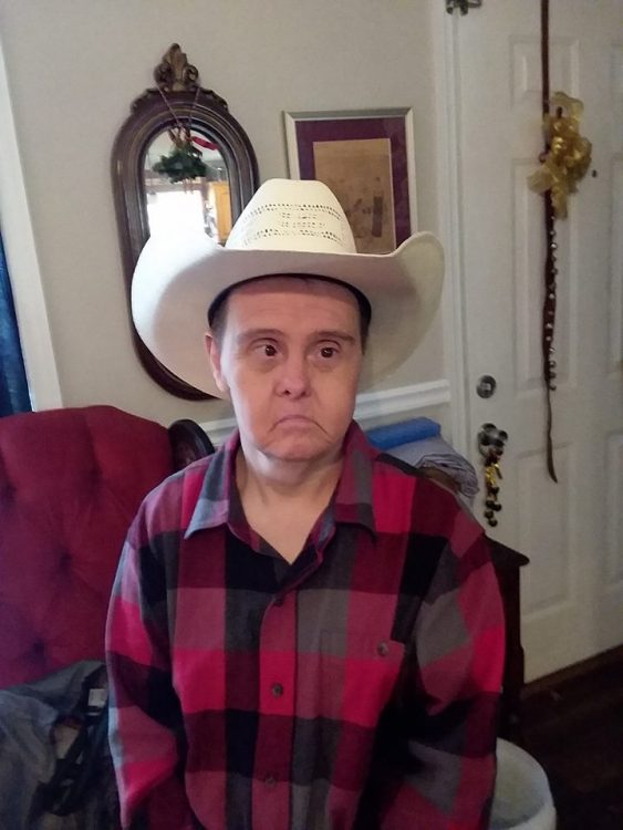 Man with Down syndrome wearing a flannel shirt and cowboy hat looking at camera without smiling.