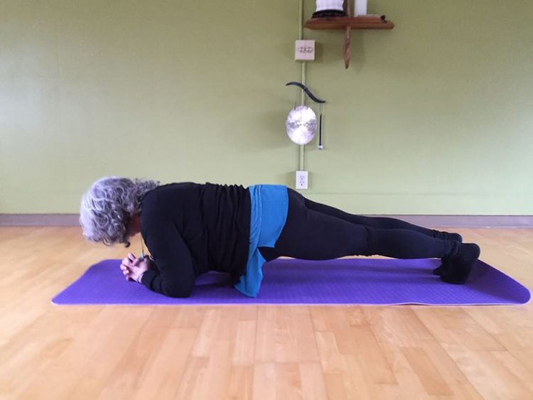 woman doing a plank on a yoga mat in a yoga studio