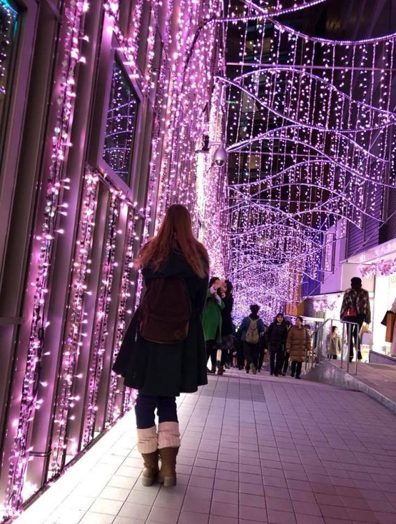 woman walking outside among christmas lights with her legs bending to the left