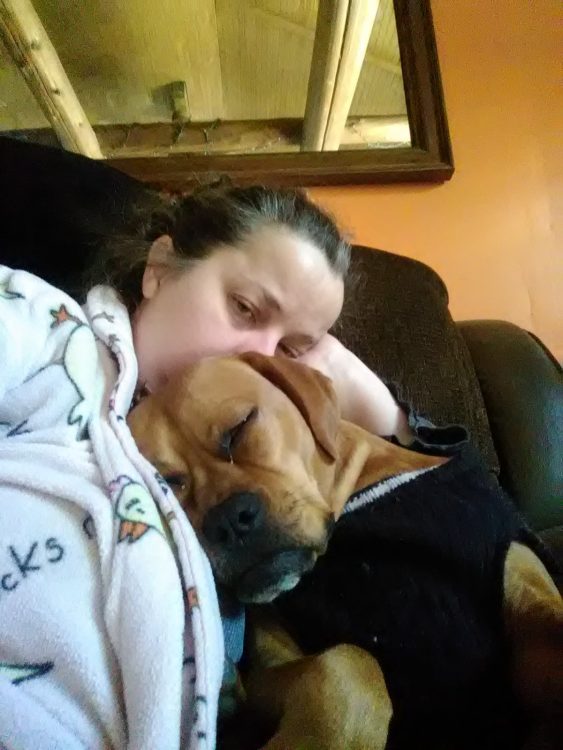 woman lying with dog on couch, dog's head on her chest