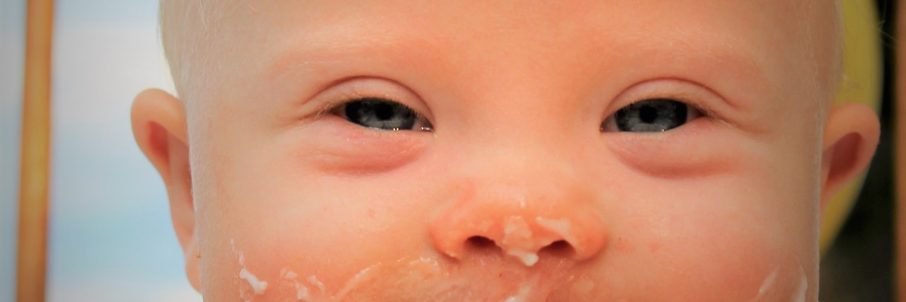 Close up of face of baby with Down syndrome with frosting on her face
