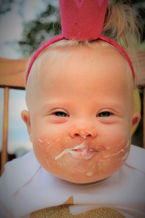 Close up of face of baby with Down syndrome with frosting on her face