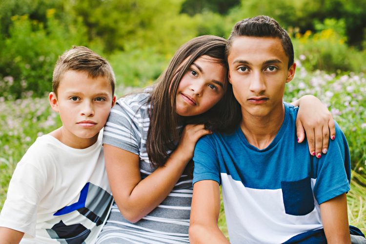 Girls with down syndrome sitting between her borters, She is leaning her head on one of her brother's shoulders