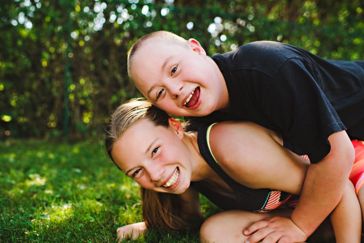 Brother and sister. They both smile at camera, brother with down syndrome is on top of sister.