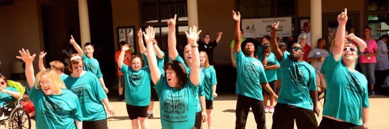 People with Down syndrome wearing green shirts and dancing in unison, arms up high, powerful