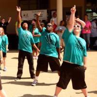 People with Down syndrome wearing green shirts and dancing in unison, arms up high, powerful