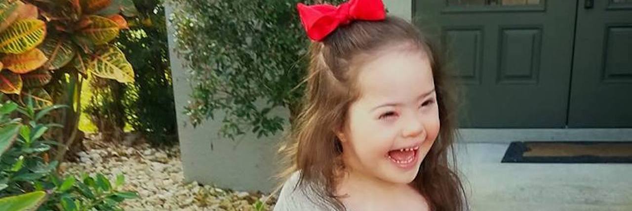 Little girl with Down syndrome standing outdoors smiling