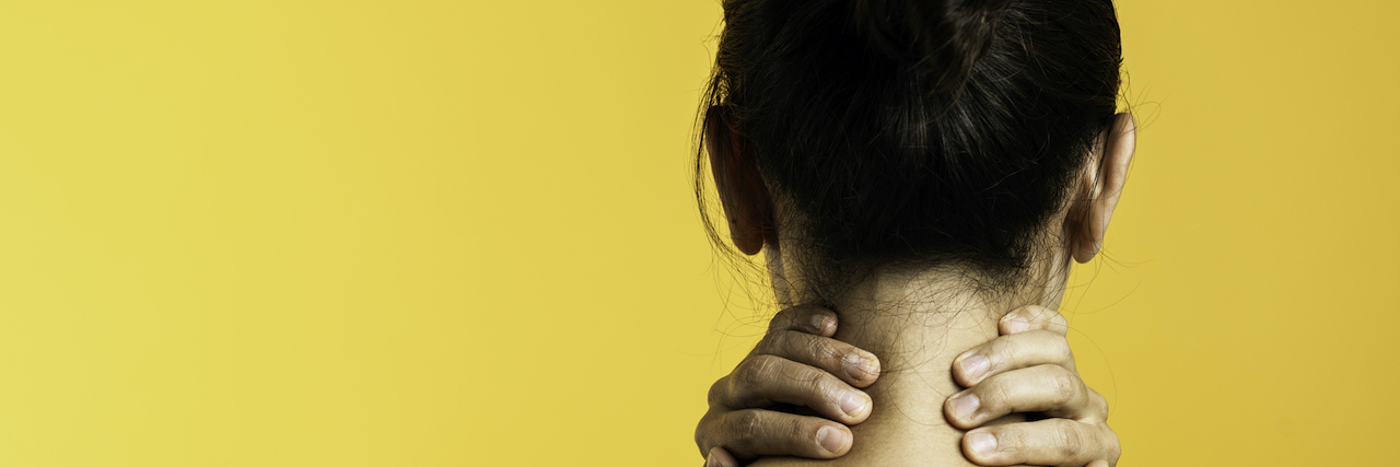 Back view of woman holding her neck in front of yellow background