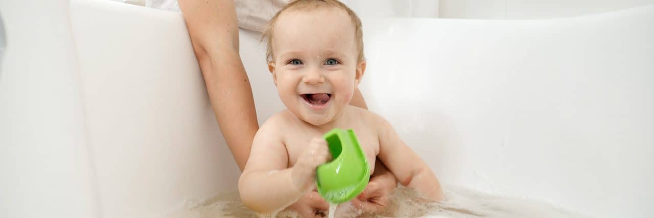 Turning My Pain Into Gratitude as I Parent My Son With Complex Needs Toddler playing in bath with parent's arms around them.