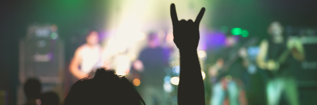 Heavy Mental Songs That Are Helping Me Deal With Depression small rock music concert with focus on fan raising horns symbol into air
