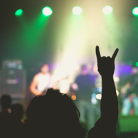 small rock music concert with focus on fan raising horns symbol into air