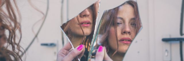 Woman looking at herself in a broken mirror