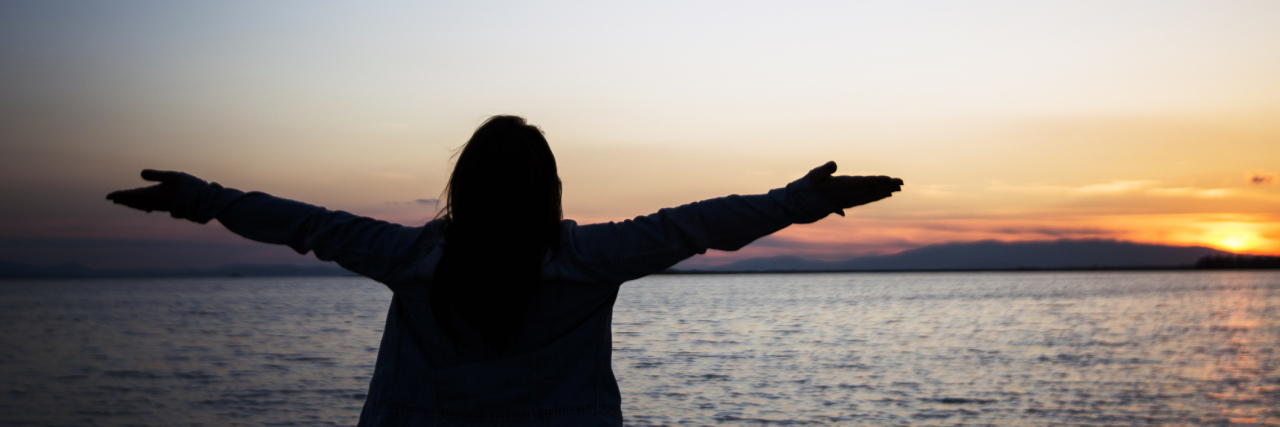 woman with her arms open against the water at sunrise