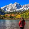 A woman admiring the autumnal beauty of the snowcapped Maroon Bells and the colorful foliage of the aspen groves on a sunny, cloudless day.