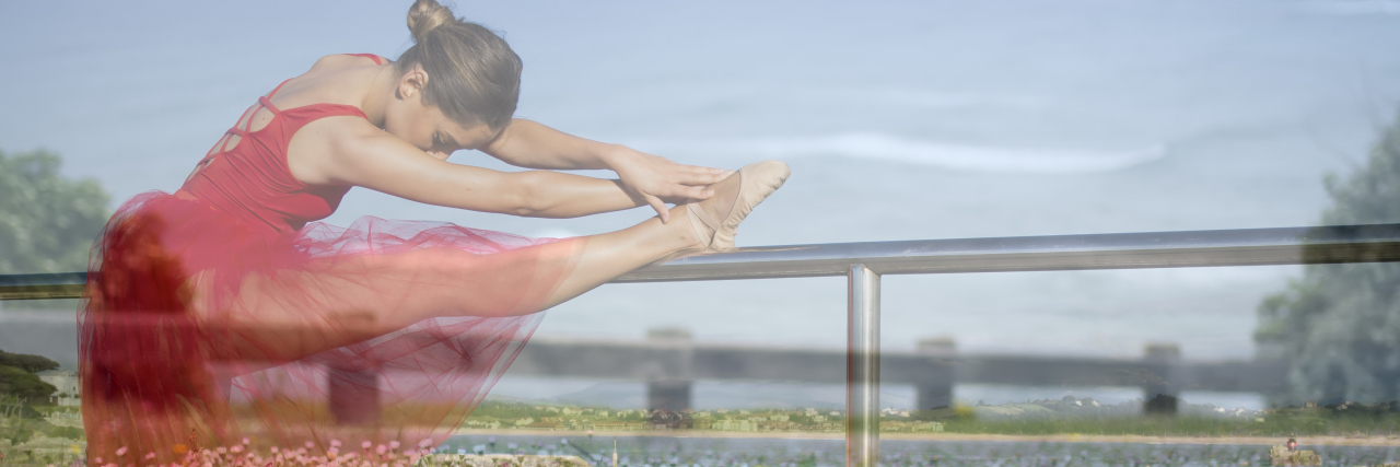 Faded image of ballet dancer stretching by the water.