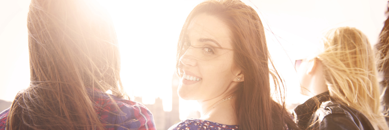 Thank You for Loving Me Through My Illness Friends walking outside, the friend in the middle looking back at the camera.