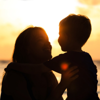 silhouette of loving mother and little son at sunset beach