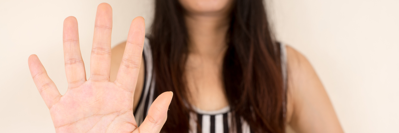 Responding to Intrusive Questions About Disability Young woman holding her hand up to say "no."