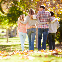 Rear View Of Family Walking Through Autumn Woodland With Arms Around Each Other