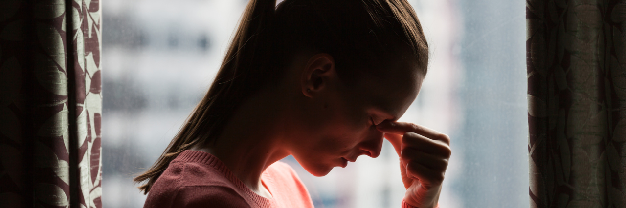 A woman with her hand to her head, looking tired or in pain.