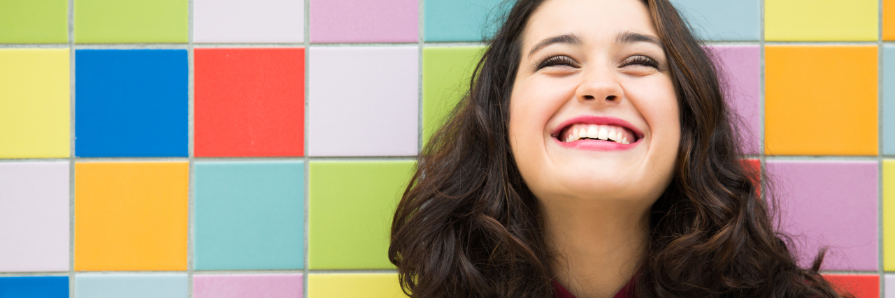 How I'm Living My Best Life With Mental Illness This Year Happy girl laughing against a colorful tiles background. Concept of joy