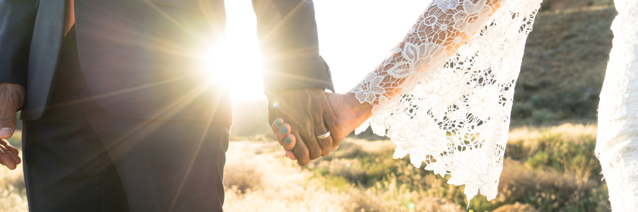 An Interracial couple holding hands backlit by the flaring sun