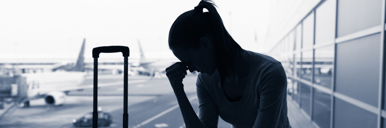 A stressed out silhouette of a woman at an airport with an airplane blurred behind her.