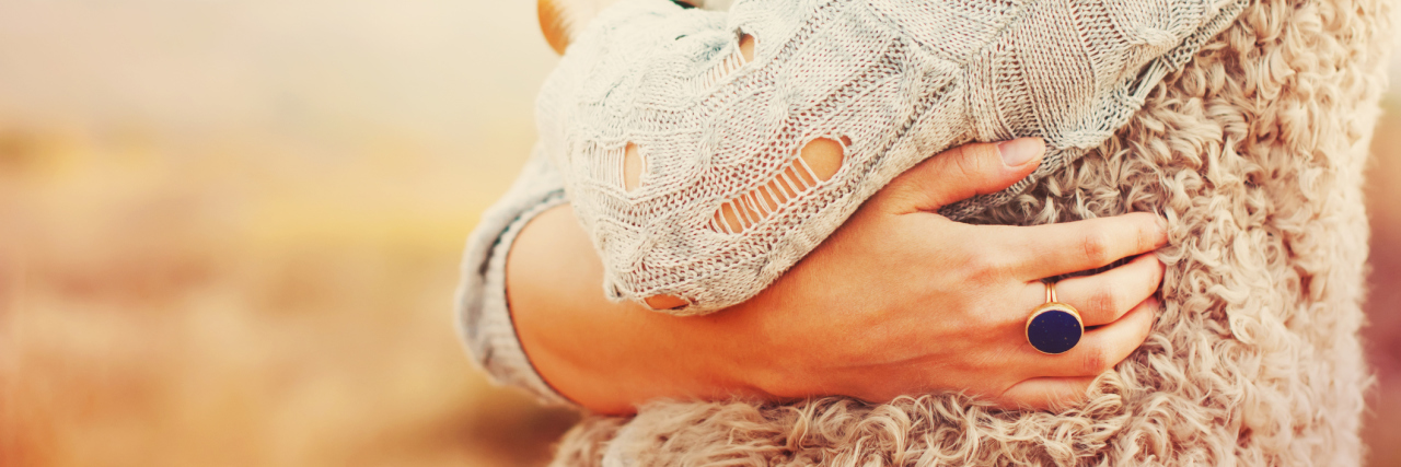 Forgiving and Accepting Lyme Disease In Order to Heal woman standing outside in a field and hugging herself