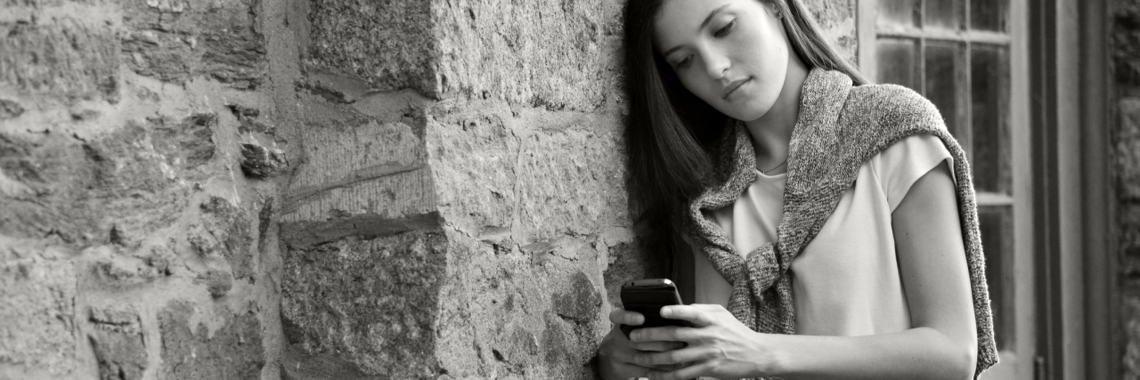 What You Need to Remember If Social Media Impacts Your Depression black and white photo of young woman on smartphone social media leaning against stone wall