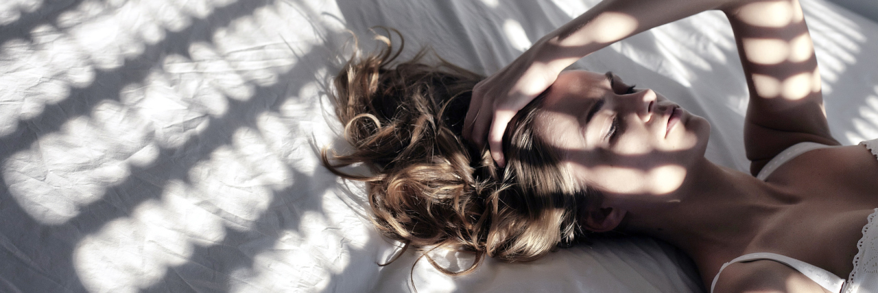 Learning to Accept the Limitations That Come With Chronic Illness woman lying on her bed with her hand on her head and shadows across her